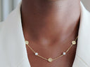 Amara Floral Pearl Station Necklace – Gold or Silver- A close-up of a person's neck wearing a delicate gold chain necklace with small white pearls and circular gold medallions, styled with a white collared shirt.