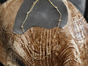 A delicate gold chain anklet with small bead accents draped over a textured brown and beige shell on a dark grey stone stand.