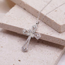 Radiant Cross Necklace – Sterling Silver | Rhodium-Plated. A silver cross pendant necklace paved with small clear stones, resting on stacked beige stone blocks.