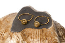Amina Lantern Hoop Earrings- A pair of gold hoop earrings with textured, spiral-patterned ball drops, displayed on a dark stone slab resting on a natural wood shell against a white background.