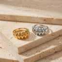 Sculpt Statement Ring- Two textured ring bands, one gold and one silver, displayed on stacked beige travertine stone slabs.