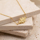 A delicate gold leaf pendant BRACELET resting on stacked beige stone tiles.