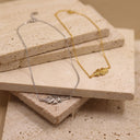 Nature Inspired Necklace. Two delicate necklace chains with matching leaf-shaped pendants, one in silver and one in gold, displayed on stacked beige stone tiles.
