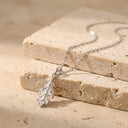 Sculpted Leaf Pendant Necklace - Sterling Silver. A silver leaf pendant necklace resting on stacked beige stone blocks against a matching stone surface.