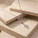 Sculpted Leaf Pendant Necklace - Sterling Silver. A silver leaf pendant necklace on a delicate chain, displayed on stacked beige stone tiles.