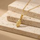 Sculpted Leaf Pendant Necklace - Sterling Silver. A gold leaf pendant necklace resting on stacked beige stone blocks against a warm beige background.