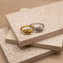 Leaf Open Band Ring – Sterling Silver. Two leaf-shaped rings, one in yellow gold and one in silver, displayed on stacked beige stone tiles.
