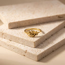 Leaf Open Band Ring – Sterling Silver. A gold leaf-shaped ring displayed on a stack of textured beige stone tiles.
