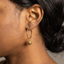 Amina Lantern Hoop Earrings- A close-up side profile of a person wearing a gold hoop earring with a dangling textured gold bead, shown on dark skin with black hair.