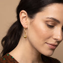 Amina Lantern Hoop Earrings- A close-up of a woman wearing a delicate gold hoop earring with a small spherical bead featuring horizontal textured lines.
