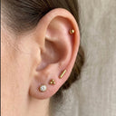 Close-up of an ear with gold and CZ  stud earrings on a neutral background