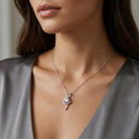 Elia Moissanite Twist Necklace – 1ct VVS | 925 Sterling Silver. A close-up of a woman wearing a delicate silver necklace with a small pendant featuring a clear round gemstone, styled with a satin gray top.