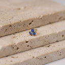 Sapphire Trio Piercing Stud- A small gold ring with three round blue gemstones, displayed on a textured beige stone slab.