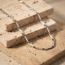 Sculpted Link Necklace – PVD Gold-Plated | Stainless Steel. A silver-toned geometric link chain necklace draped over stacked beige travertine stone tiles.