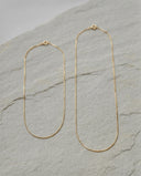 Two gold-toned chain necklaces with elongated oval shapes, displayed on a textured light grey stone surface.