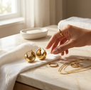 Gold jewellery including earrings and a necklace on a marble surface with a hand reaching out.