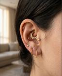 Close-up of an ear with multiple gold earrings in a home setting