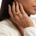 A close-up lifestyle shot of a model wearing a chunky, Sculpt Statement Ring on her finger, with her hand resting near her ear. She is wearing a white satin blouse against a clean white background.