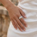 Sculpt Statement Ring - A close-up of a person's hand wearing a textured silver ring, resting on a white satin dress with a blurred outdoor background.