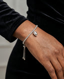 A close-up of a person's wrist wearing a silver beaded bracelet with a small acorn charm and dangling chain accents, paired with a black velvet long-sleeve top.