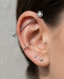 Close-up of an ear with multiple silver earrings on a neutral background