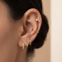 Close-up of a model's ear showcasing multiple gold ear piercings, Star & Bar CZ Cartilage Stud a small stud, a curved hoop, a huggie hoop, a pavé huggie, and a pavé barbell cartilage piercing.