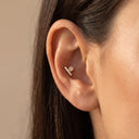 A close-up of a model's ear wearing Star & Bar CZ Cartilage Stud set against a soft beige background.