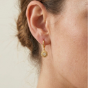 Gold sunflower earring worn by a person on a neutral background