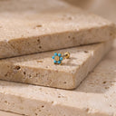 Himari Sunflower Piercing Stud- A small gold flower-shaped stud earring with turquoise blue stones, resting on a beige stone slab.