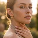 Ayra Twist Hoop Earrings- A close-up portrait of a woman outdoors at golden hour wearing a small textured gold hoop earring.