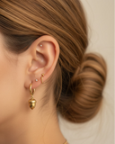 Close-up of a person wearing gold hoop with an acorn charm earrings with a neutral background