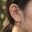 Close-up of a person's ear with multiple earrings against a blurred natural background