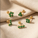 Gold earrings with emerald green gemstones on a beige fabric background