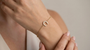 Gold bracelet with a horse shoe charm on a wrist against a neutral background