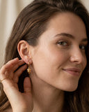 Close-up of a woman wearing gold Acorn Huggie Hoop earrings with a neutral background