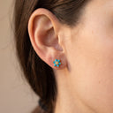 Himari Sunflower Piercing Stud- A close-up of a person's ear wearing a small flower-shaped stud earring with turquoise blue stones and a gold center.