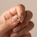 Floral Vine CZ Cartilage Piercing Stud- A close-up of a hand with manicured nails holding a small gold flower ring with clear gemstones against a soft beige background.