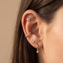 Flora CZ Flower Piercing Stud. Close-up of a person's ear showcasing multiple gold and silver stud earrings.