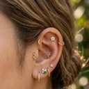 Close-up of an ear with multiple gold earrings against a blurred natural background