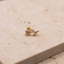 Floral Vine CZ Cartilage Piercing Stud A small gold stud earring with a flower and leaf motif set with clear stones, resting on a textured beige stone surface.