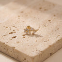 Floral Vine CZ Cartilage Piercing Stud- A small gold flower-shaped stud earring with clear gemstones, resting on a textured beige stone slab.