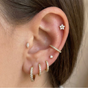 Close-up of an ear with multiple gold earrings on a neutral background