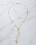 A delicate gold chain necklace with a Y-shaped drop design and small teardrop pendants, displayed on a white marble surface.