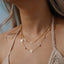 Layered look of the clover gold necklaces on a model wearing a crochet top.
