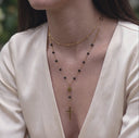 Waterproof rosary inspired cross necklace for women- A close-up of a woman wearing a layered gold necklace with small black beads and a cross pendant, paired with a cream satin top.