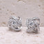 Pair of silver knot earrings with clear gemstones on a textured beige surface