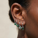 Close-up of an ear wearing three green gemstone hoop earrings.