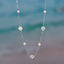Silver clover necklace with pearls against a blurred beach background