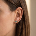 Himari Sunflower Piercing Stud - Close-up of a woman's ear wearing three gold ear piercings: a small flower stud with turquoise blue stones, a tiny white stone stud, and two curved gold hoop earrings.