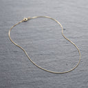 A delicate gold chain necklace with a lobster clasp, displayed on a textured grey slate surface.